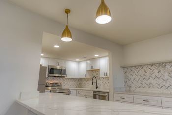 A modern kitchen with a white countertop and gold pendant lights.at The Garden District Apartments, Germantown, TN  